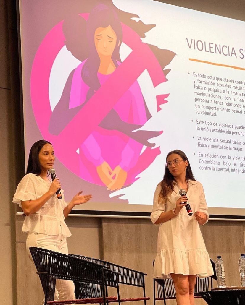 Dos mujeres con micrófono hablan en un escenario frente a una diapositiva sobre violencia sexual.
