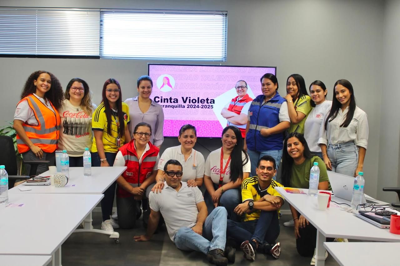 Grupo de trabajadoras y trabajadores de empresas, algunos con chalecos de seguridad, posan sonrientes junto a una pantalla en una sala de reuniones.