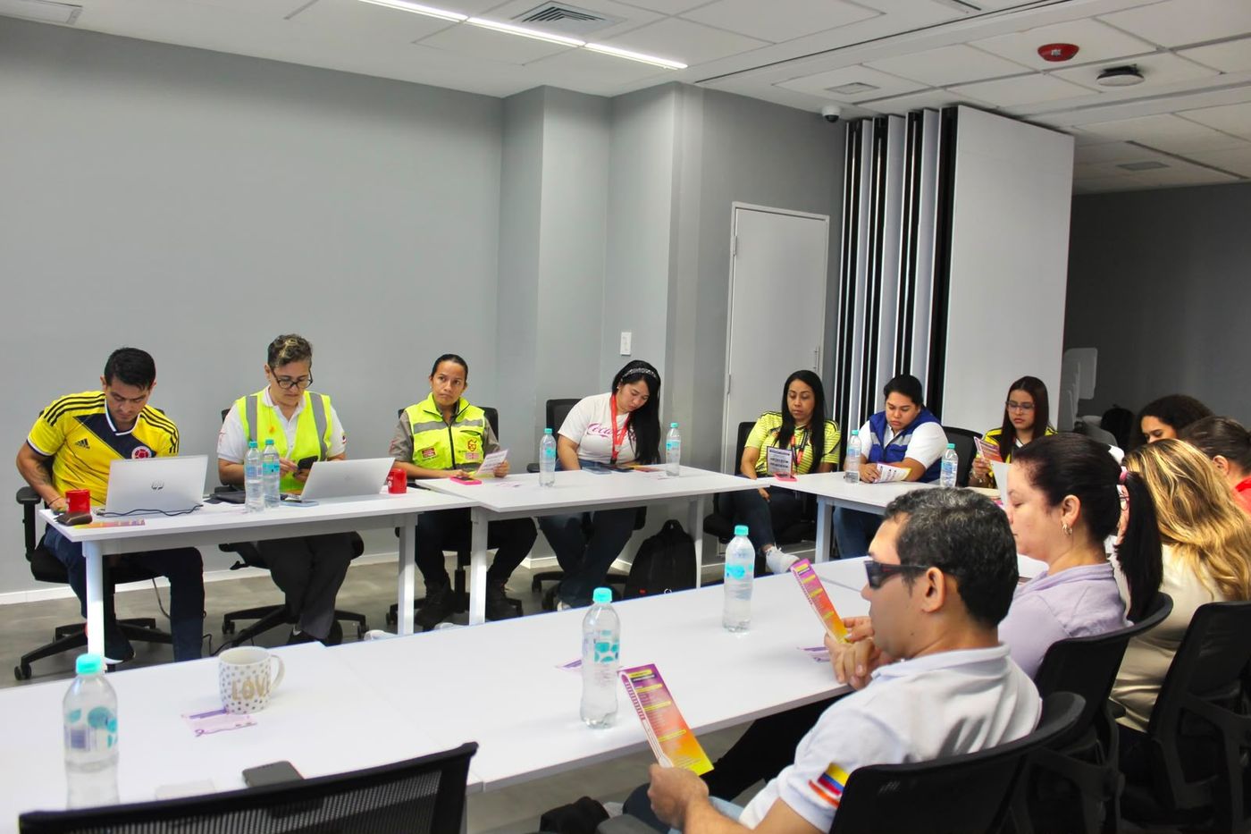 Participantes de un taller, algunos con chalecos de seguridad, leen material impreso alrededor de una mesa.